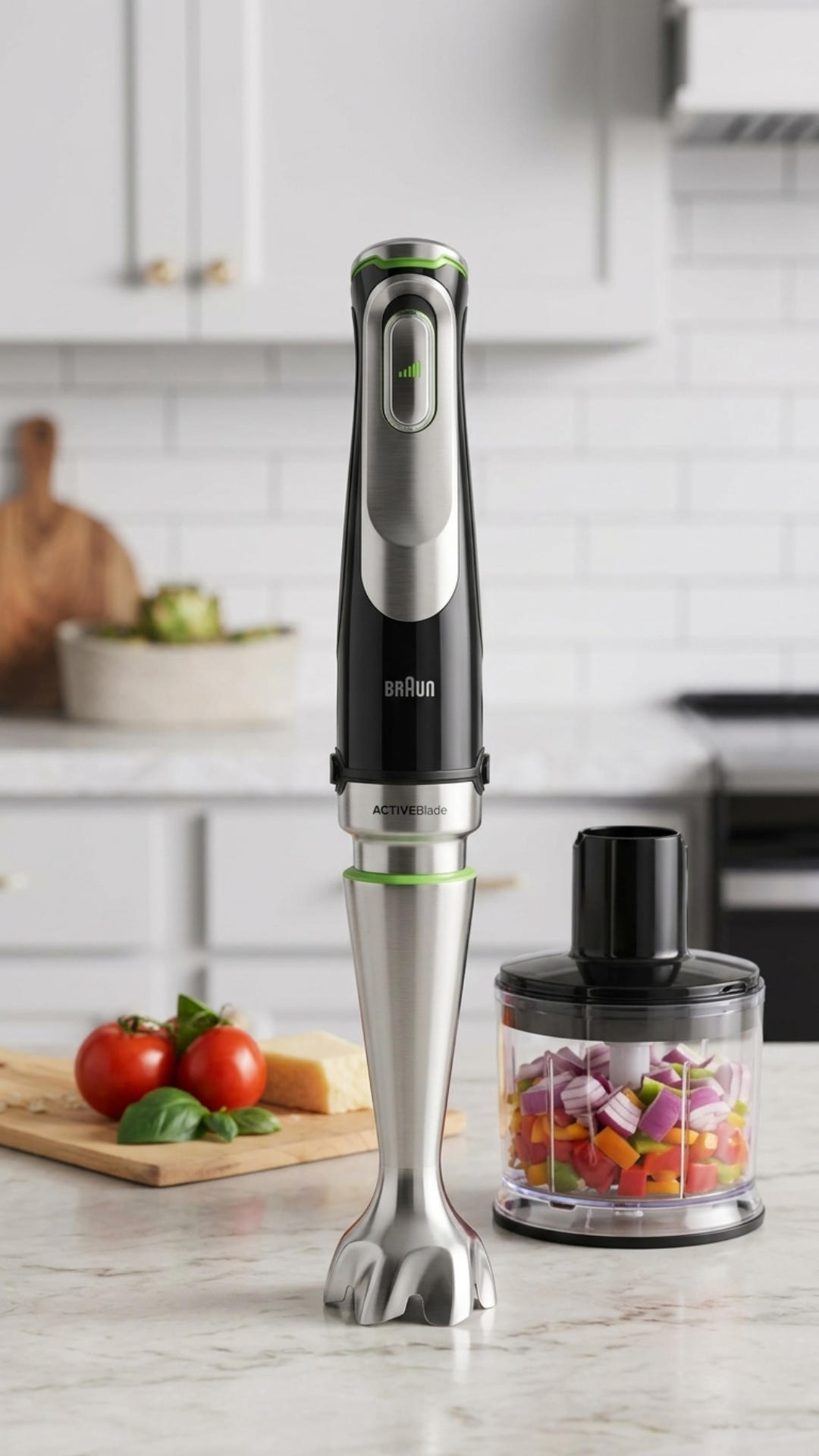 A Braun MultiQuick hand blender with a black and silver body stands upright on a marble countertop next to its clear chopper attachment filled with diced red onions and peppers. In the background, a wooden cutting board holds tomatoes and cheese in front of white kitchen cabinets.