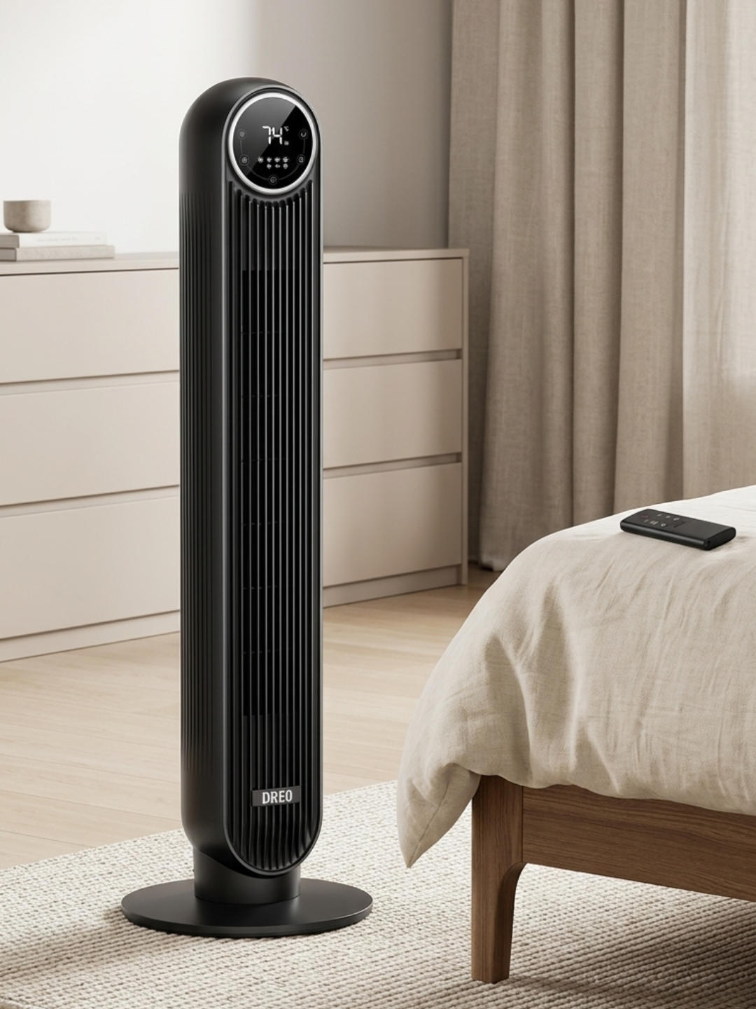 A tall, matte black tower fan stands on a light-colored woven rug next to a bed with beige linens and a wooden frame. In the background, a light wood dresser and beige drapes create a neutral, calm setting.