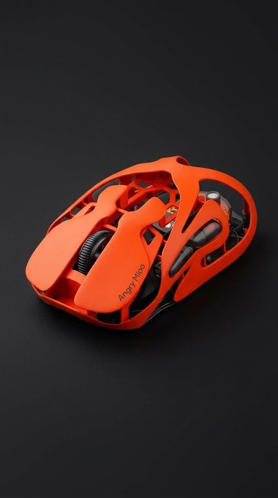 A Blaze Orange wireless gaming mouse on a light wood desk beside a black keyboard and coiled USB-C cable.