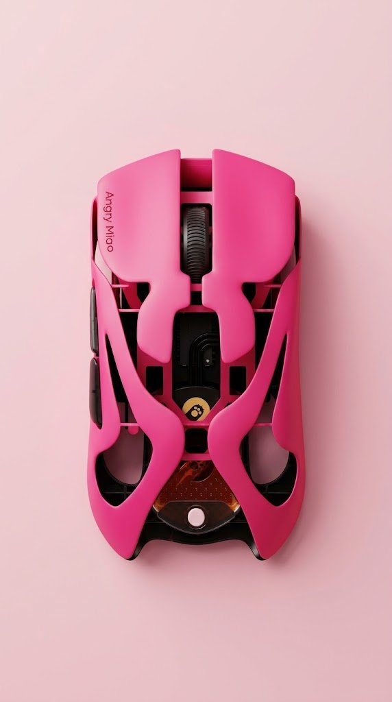 Matte pink wireless mouse resting on a light wood desk surface beside a small black charging dock and two orange cylindrical batteries.