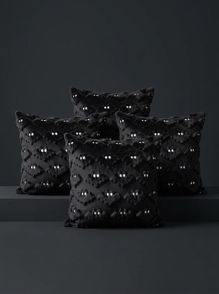 Four black square throw pillows arranged against a dark gray background, featuring raised textured bat silhouettes with tiny white embroidered eyes.